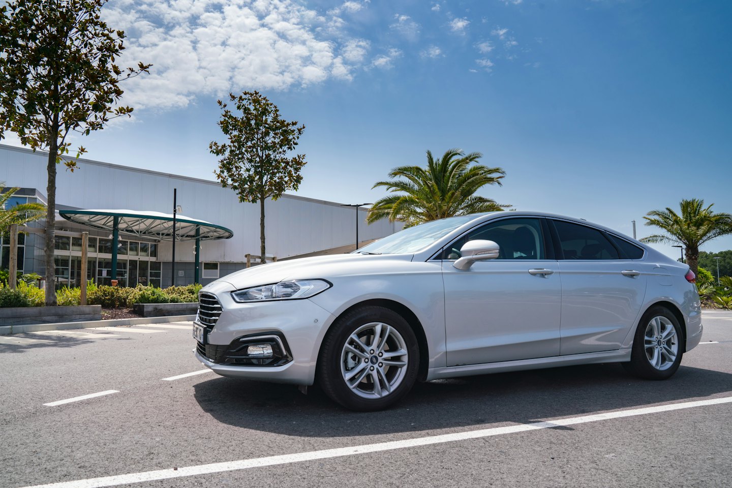 Berline argentée garée sur un parking en asphalte près d'un bâtiment blanc moderne.
