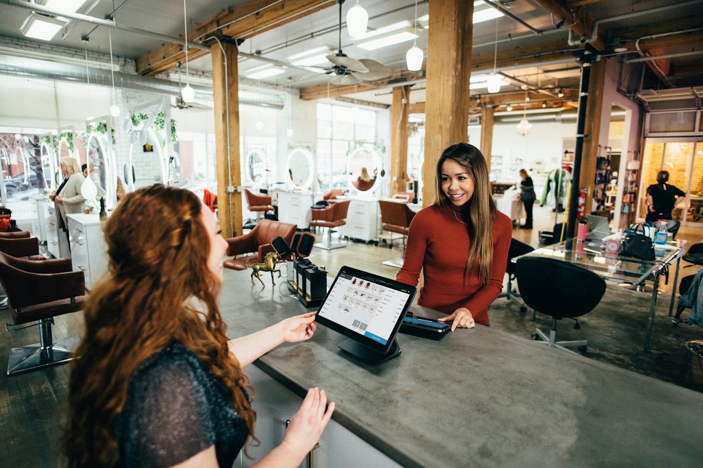 Une vendeuse montre une sélection d'articles sur une tablette à un client, derrière le comptoir.